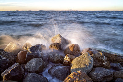 Waves splashing on rocks at shore during sunset