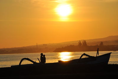 Silhouette man on shore against orange sky