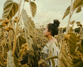 Close-up of young woman standing by plants in field