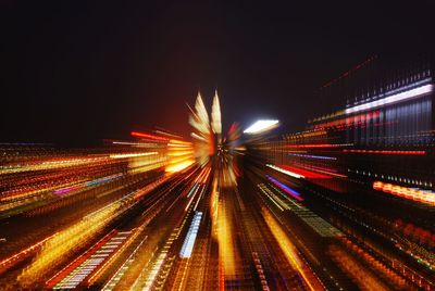 Light trails on illuminated city against sky at night