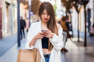 Young woman using mobile phone while standing in city