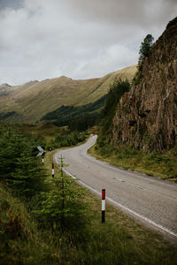 Empty road by mountains against cloudy sky