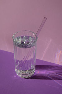 Reusable glass straws in glass with water on purple violet background eco-friendly drinking straw