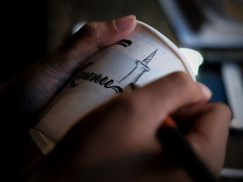 Cropped hand of woman writing on disposable cup