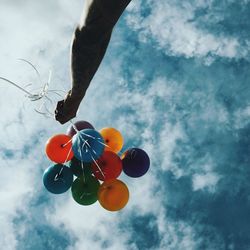 Cropped image of hand holding colorful balloons against sky