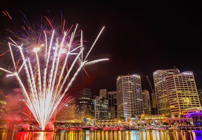 Firework display in city against sky at night
