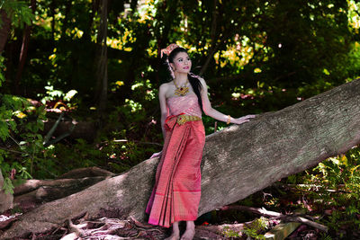 Young woman in traditional clothing looking away while standing by tree trunk at forest