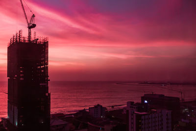 Silhouette buildings by sea against sky during sunset