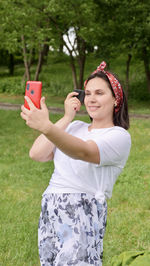 Smiling woman doing selfie on grass against trees