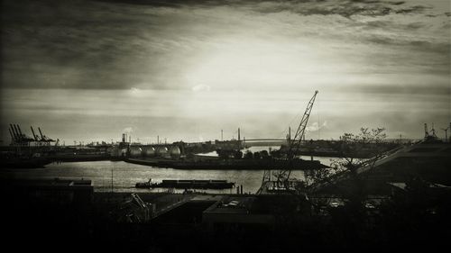 Cranes at harbor against cloudy sky