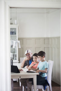 Grandfather sitting by twin grandsons reading book at table