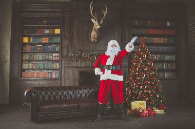 Man wearing santa claus costume standing by christmas tree at home