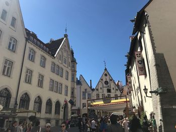 People on street amidst buildings against clear blue sky