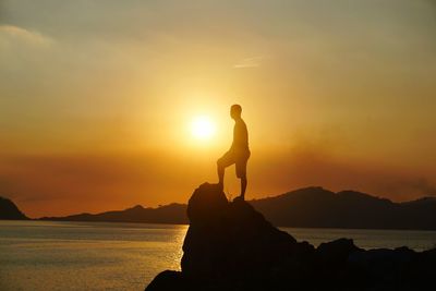 Silhouette of man standing on shore at sunset