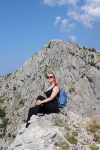 Woman sitting on rock against sky in sunny day