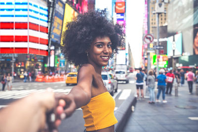 Side view portrait of happy young woman with afro hairstyle holding hand on city street