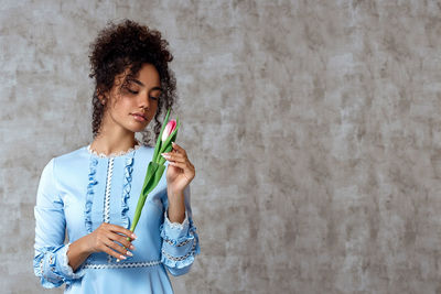 Beautiful woman holding tulip while standing against wall