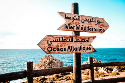 Information sign by sea against sky