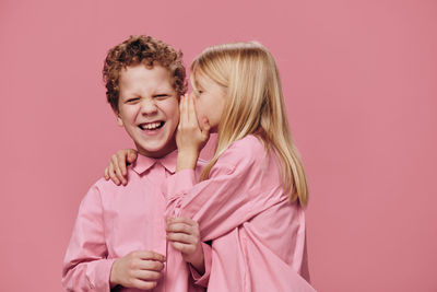 Girl whispering in boy's ear against pink background