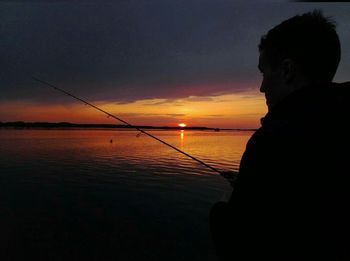 Silhouette man fishing in sea against sunset sky