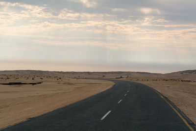 Country road on arid landscape against cloudy sky
