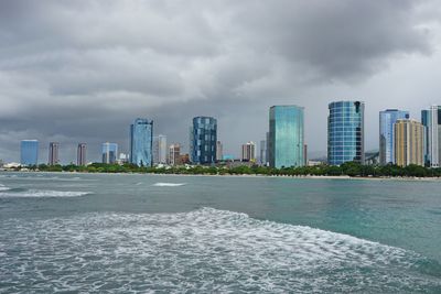 Modern buildings by sea against sky in city