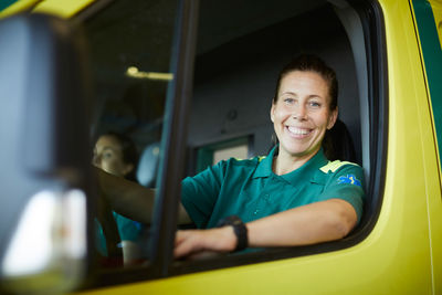 Portrait of smiling mature female paramedic driving ambulance in parking lot