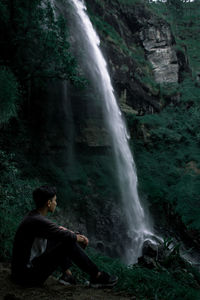 Side view of man sitting on rock in forest