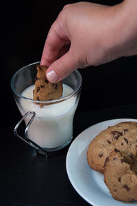 Close-up of hand holding chocolate cookie with black background