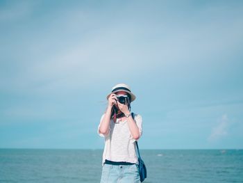 Woman photographing at beach against sky