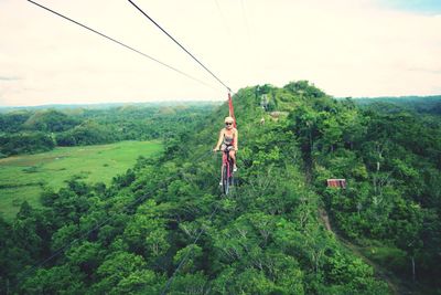 Woman riding bicycle on zip line over trees