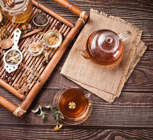 Cup of herbal tea with teapot and wooden tray with various dry herbs. top view