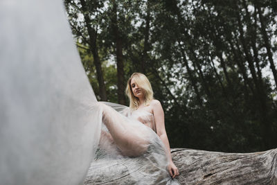 Young woman sitting on tree against plants