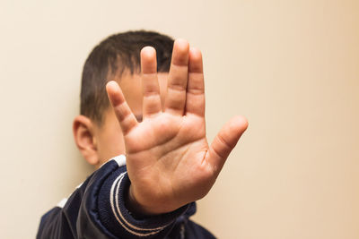 Close-up of boy showing stop gesture against beige background
