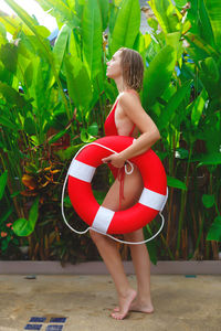 Full length of woman holding red while standing by plants