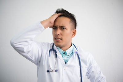 Stressed doctor standing against white background