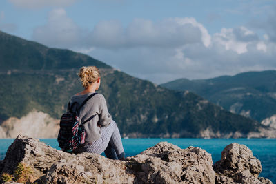 Woman sitting on rock looking at mountains against sky