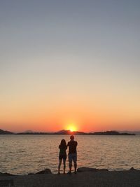 Rear view of couple at beach against sky during sunset