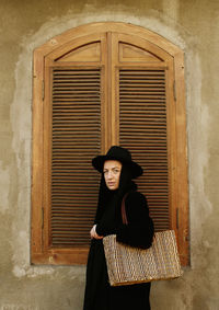 Portrait of young woman standing against wall