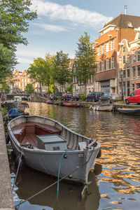 Boats moored in river by buildings against sky