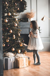 Full length of girl standing by christmas tree at home