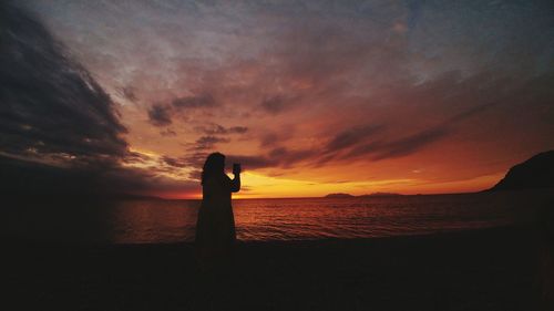 Silhouette man looking at sea against sky during sunset