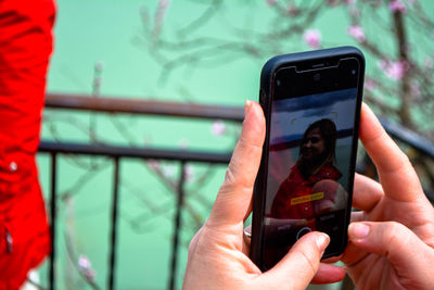 Close-up of person photographing woman through mobile phone