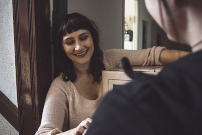 Smiling customer talking to delivery woman while holding package at doorstep