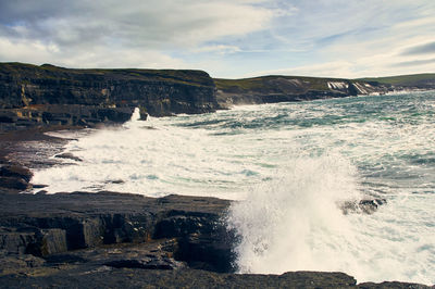 Waves splashing on rocks against sky