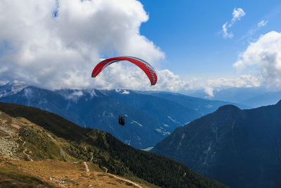 Person paragliding over mountains against sky