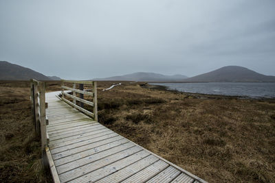 Boardwalk leading towards mountains against sky