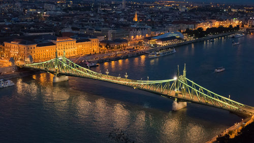 Illuminated bridge over river in city at night