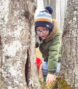 Portrait of boy standing by tree trunk