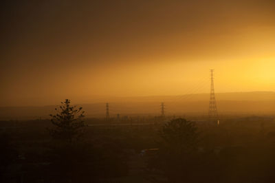 Silhouette trees and electricity pylon against sky during sunset